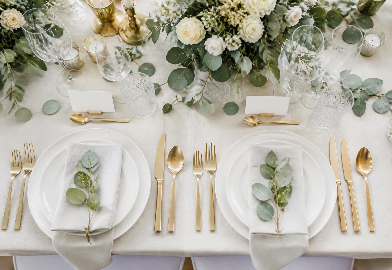 Elegant wedding reception place setting with eucalyptus, gold flatware and place cards